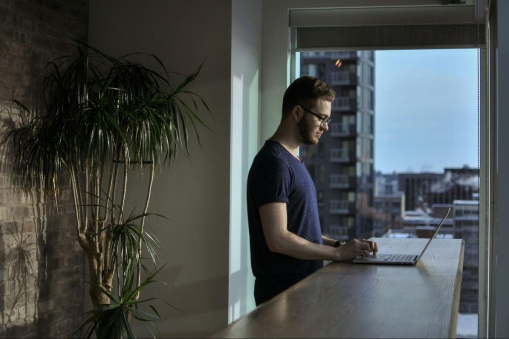 Uomo in piedi mentre lavora al suo computer portatile su un piano di lavoro