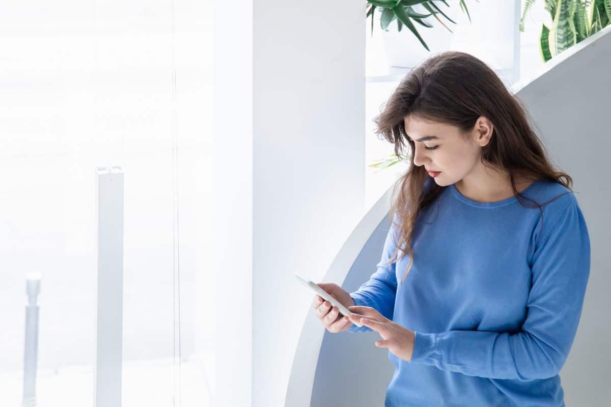 ttraktiv, seriøs ung kvinne i blå genser bruker smarttelefon