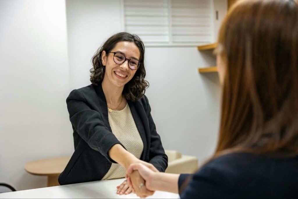 Deux femmes, souriantes, se serrent la main sur un bureau lors d'un entretien d'embauche.