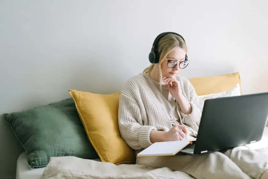 Uma mulher sentada em uma cama com um laptop e fones de ouvido