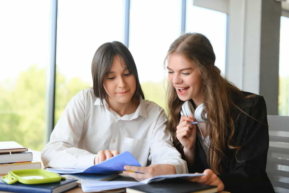 Smiling schoolgirls are talking about homework at the desk in the class
