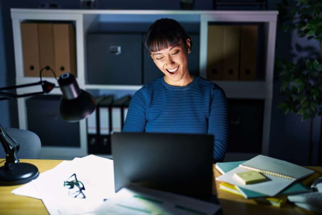 Young beautiful woman working at the office at night winking