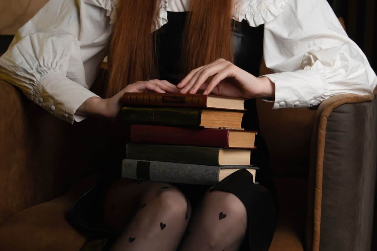 A young girl is sitting in a dark room and holding old books in her hands