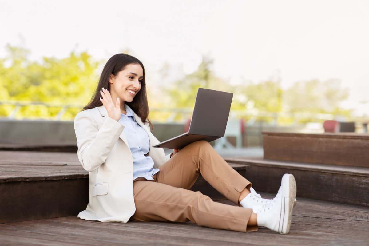 young european woman sits on ground outdoors with laptop