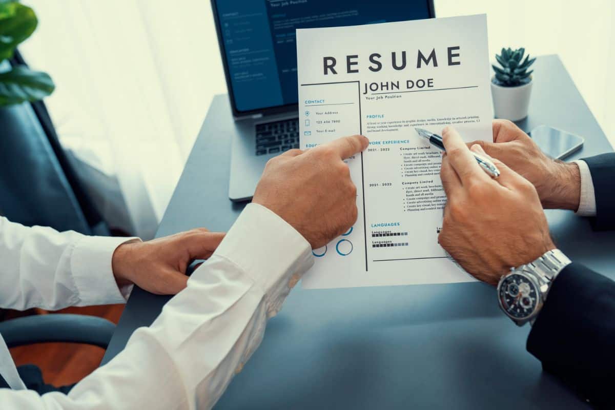 man is holding a resume in front of a laptop