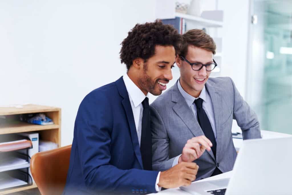 Two businessmen working together on a laptop in an office setting.