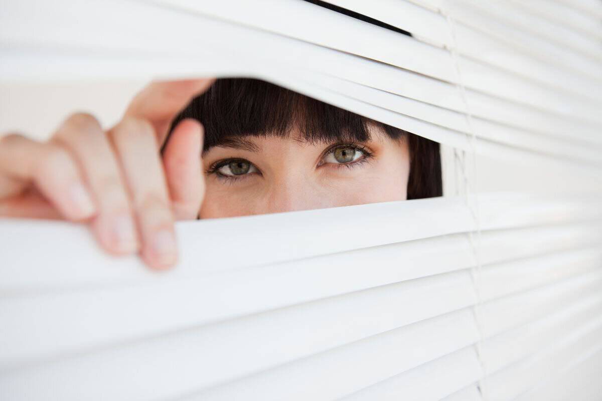 A woman looking through a closed set of blinds by opening