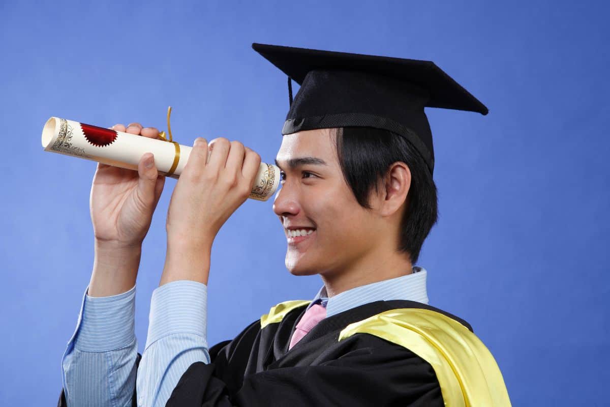 Smiling man in graduation gown looking through certificate