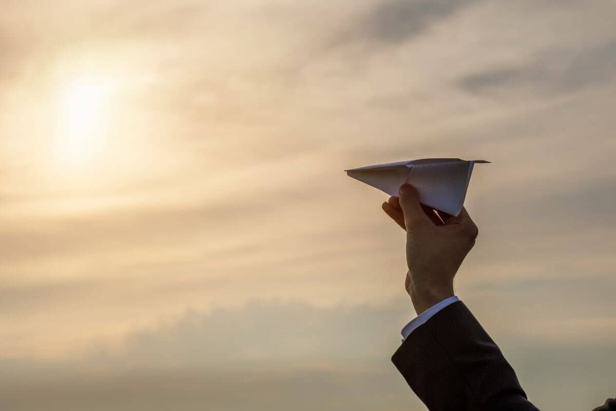 Hand launches an airplane in the direction of the sun