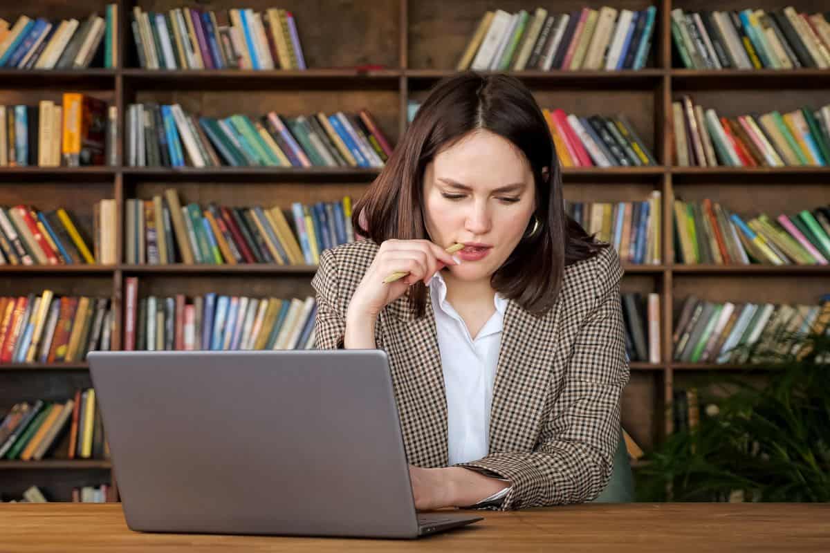 Thoughtful project manager holds pen looking into laptop