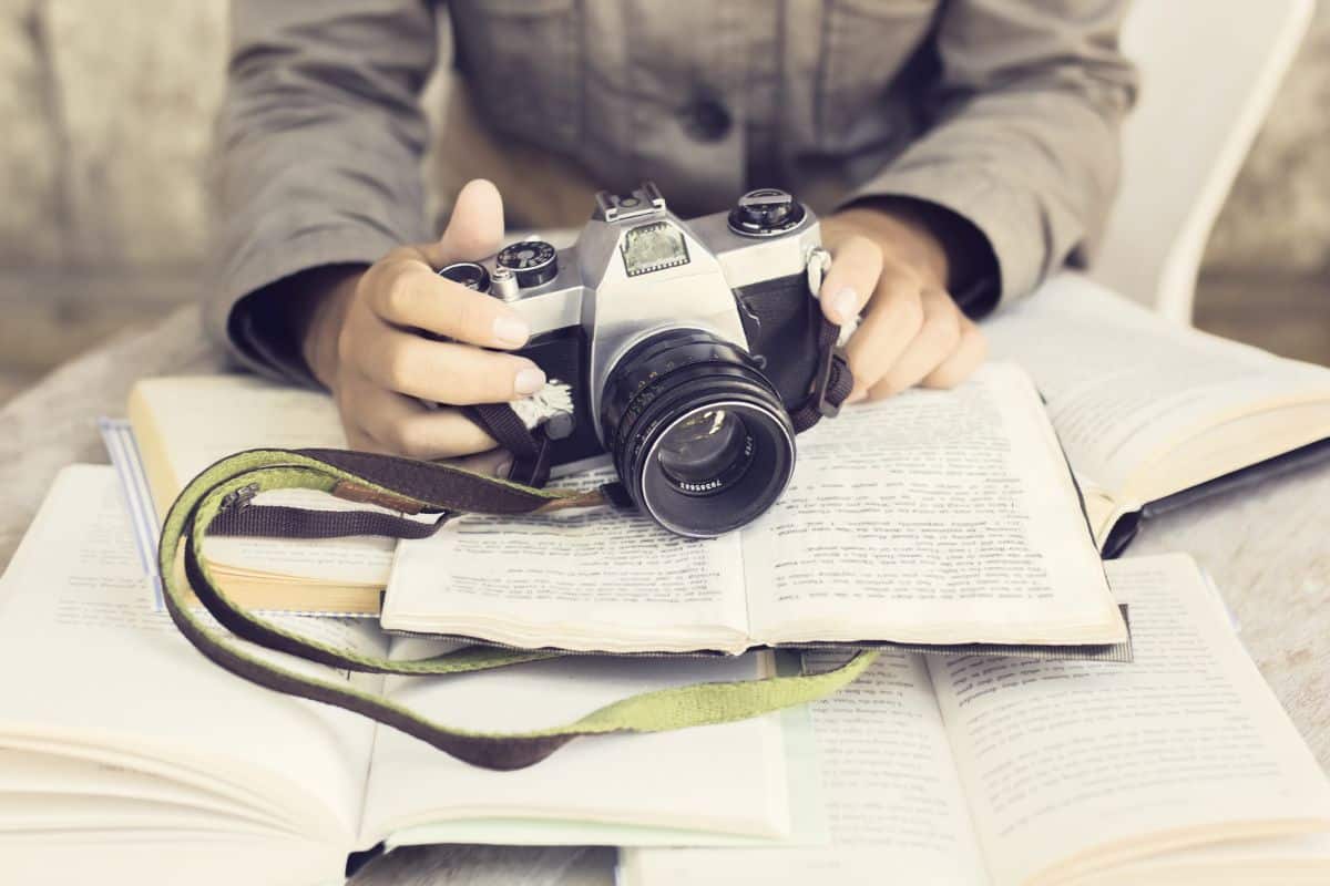 Hands with old camera and several open books on a wooden table