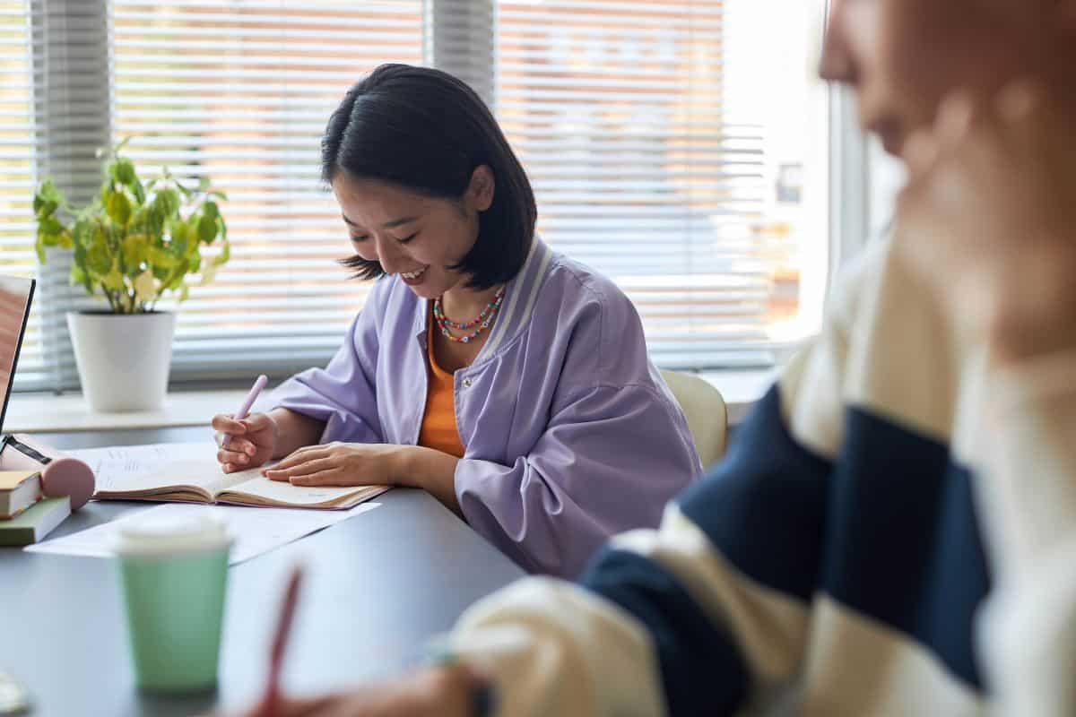 Happy young asian brunette woman looking through test questions on paper