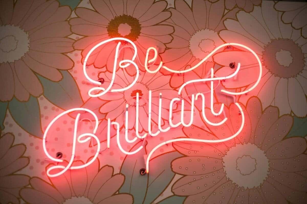 Zdjęcie stockowe przedstawiające frazę "Be Brilliant" świecącą w neonach na kwiecistym tle.