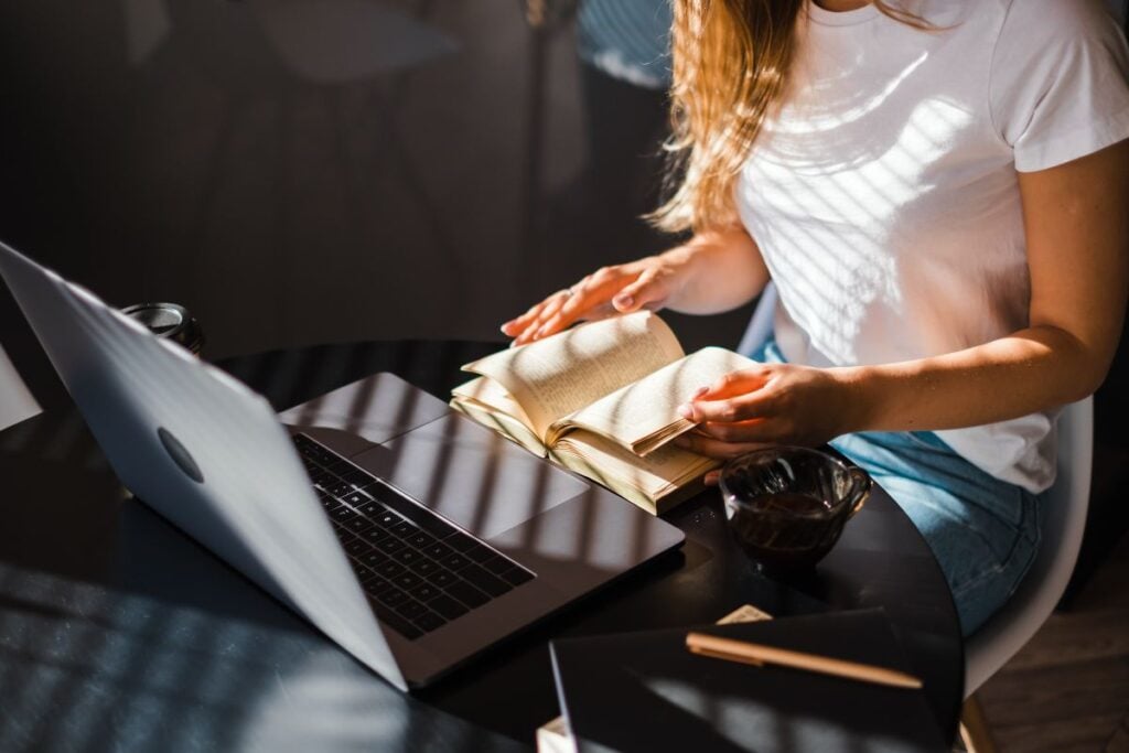 woman reading book in front laptop at the kitchen