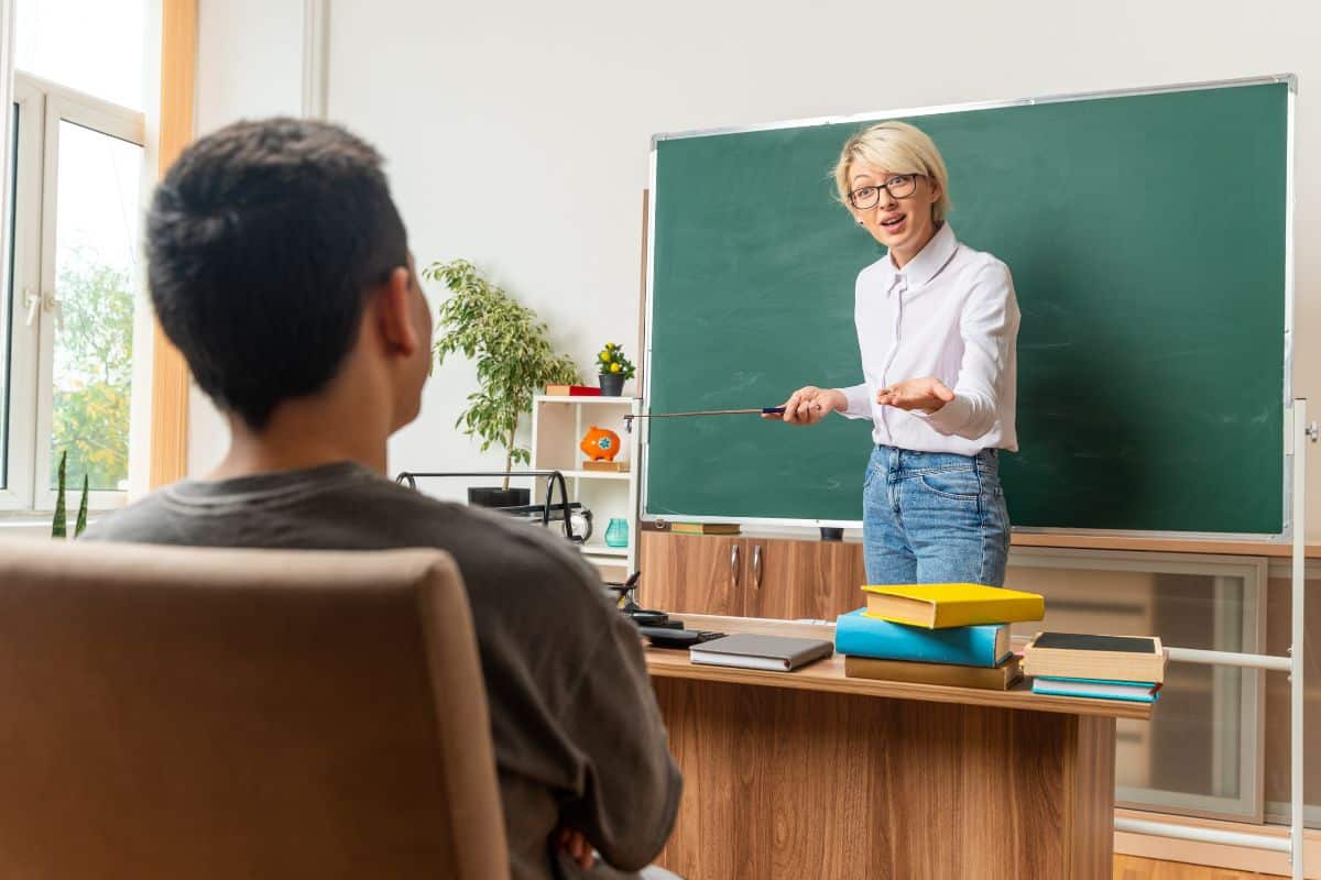 Excited young blonde female teacher wearing glasses in classroom