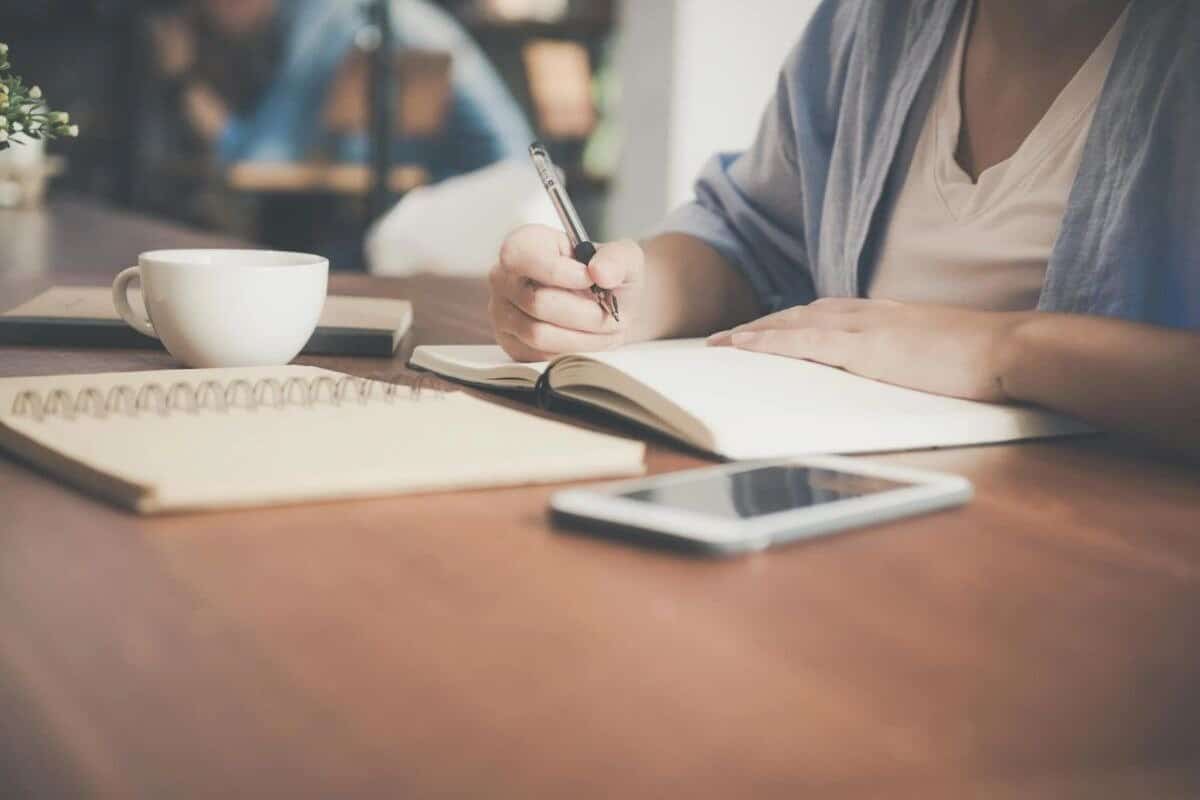 Osoba píšící do notebooku, vedle ní stůl a hrnek s kávou.