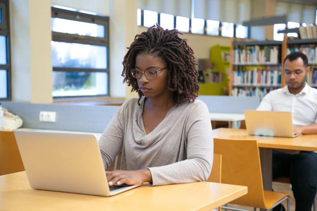 Concentrated young woman working with laptop at library