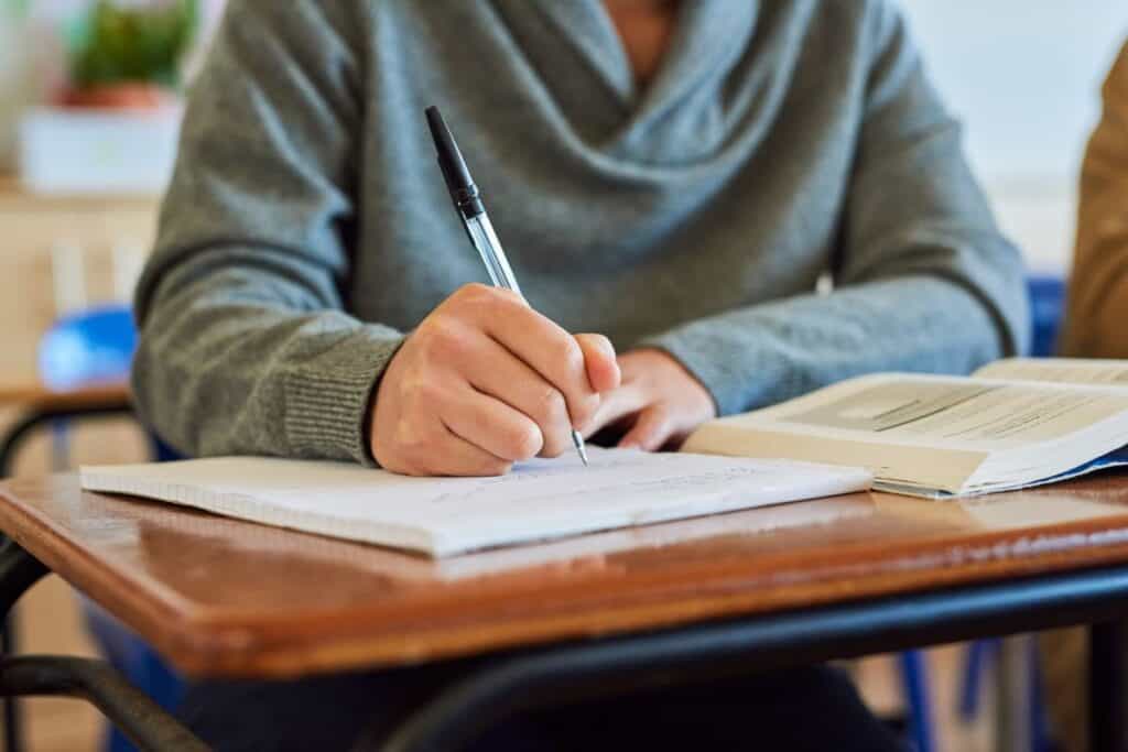 University student hand and writing in classroom with books