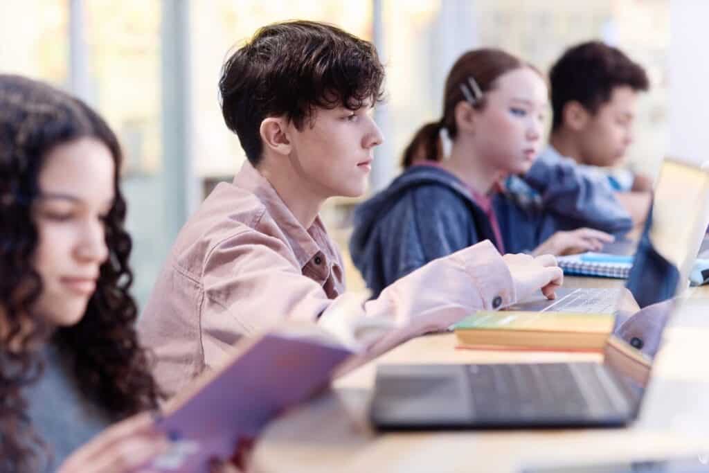 Estudante acusado falsamente por detectores de IA 7 Boy using computer in library with students in row