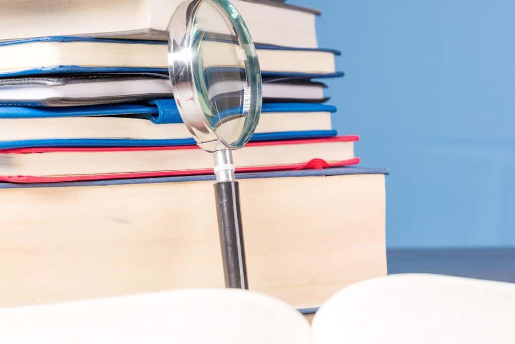 Stack book with magnifying glass on wooden desk in information library