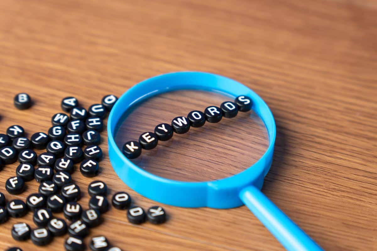 A blue magnifying glass with alphabet beads that spell out keywords