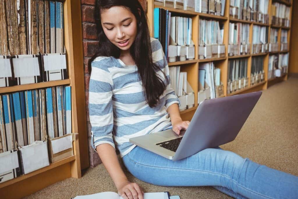 Smiling student sitting on the floor against wall in library