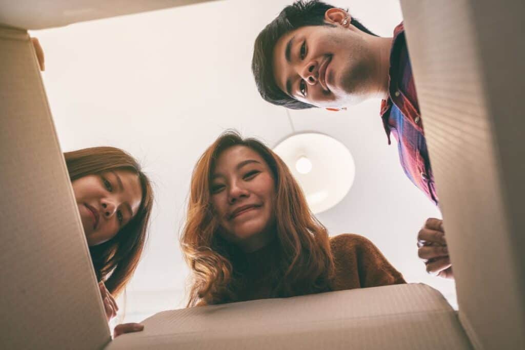 O que são preposições? Guia gramatical + exemplos 5 Group of young people opening and looking for a gift in the box