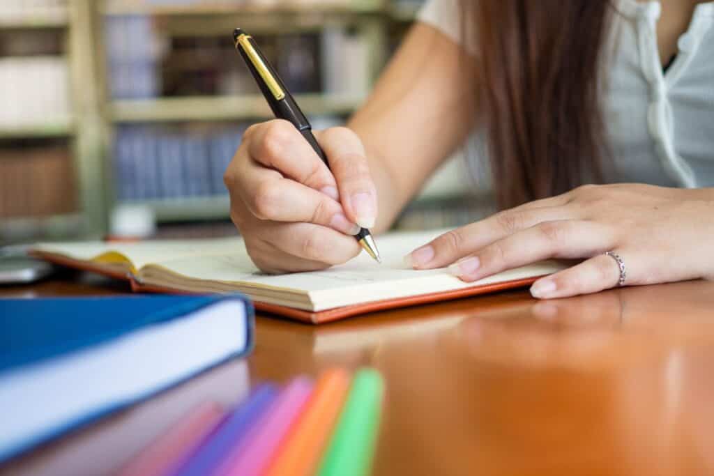 Female student writing book inside the library