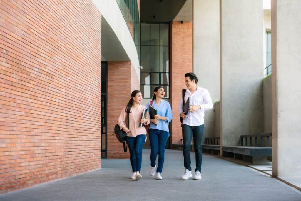 Asian three students are walking and talking together in university hall