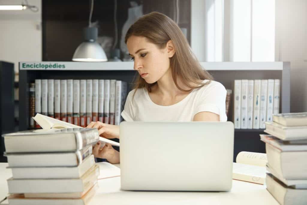 Woman studying with books and laptop in a library or study space.