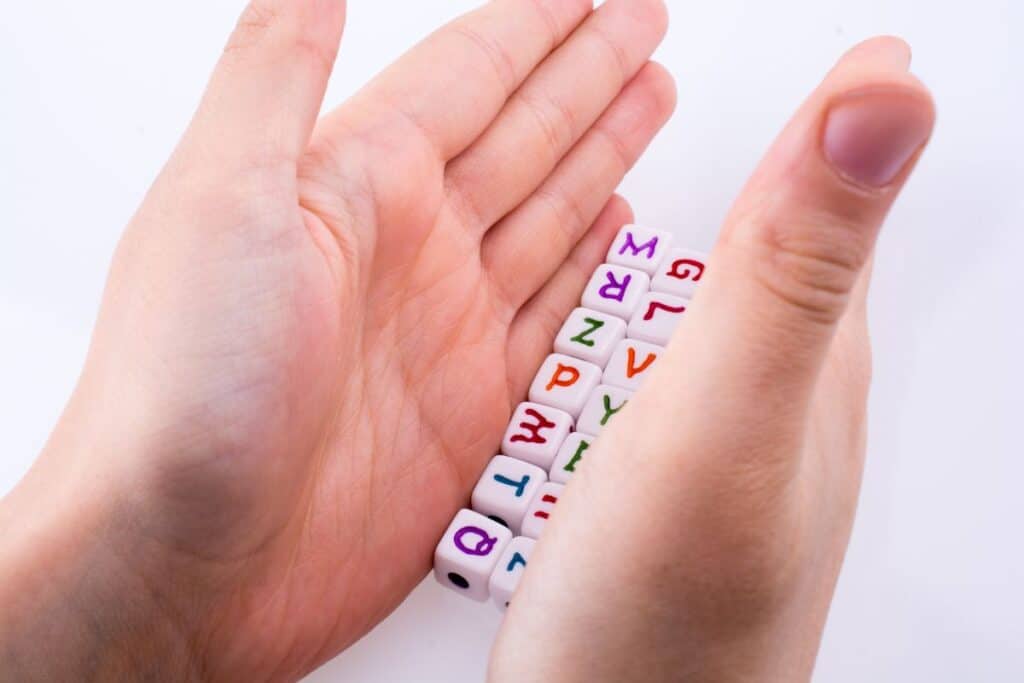 Qu'est-ce qu'une consonne ? Guide complet et exemples 5 Hand playing with letter cubes on a white background