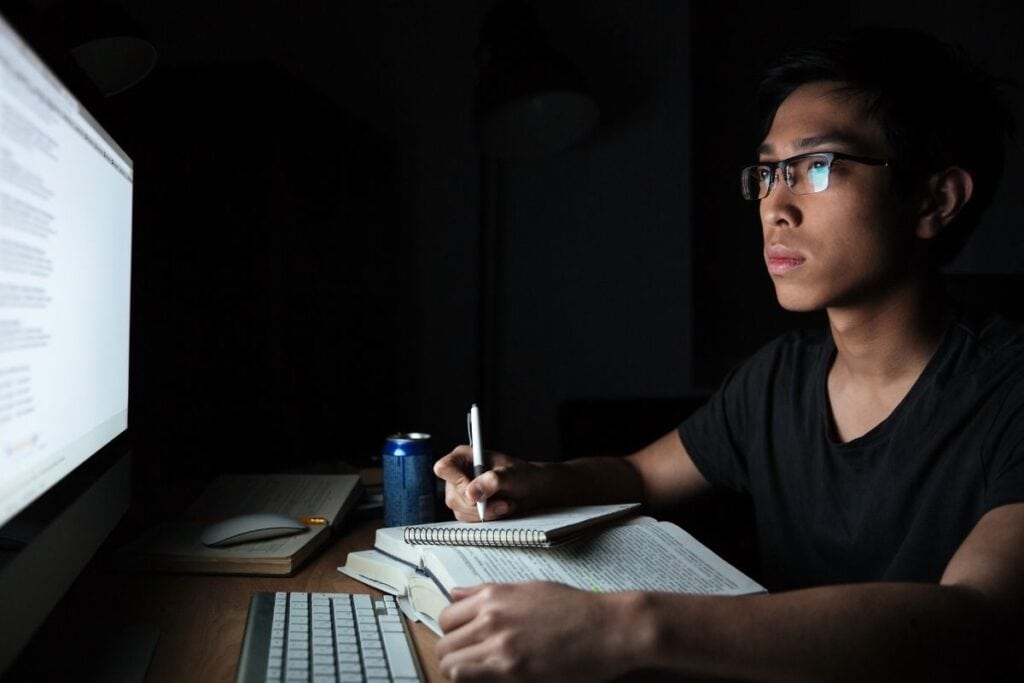 Concentrated asian young man writing in notepad 