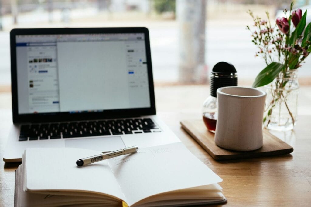 MacBook Pro di dekat buku terbuka berwarna putih
