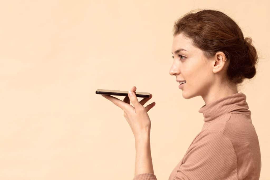 Como detectar áudio de IA usando nosso guia de detecção de voz de IA 8 Mulher falando no alto-falante do celular