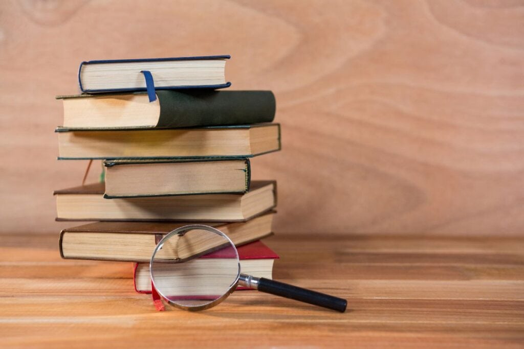 Como citar fontes usando um gerador de citações APA Guia 7 Lupa com uma pilha de livros sobre uma mesa