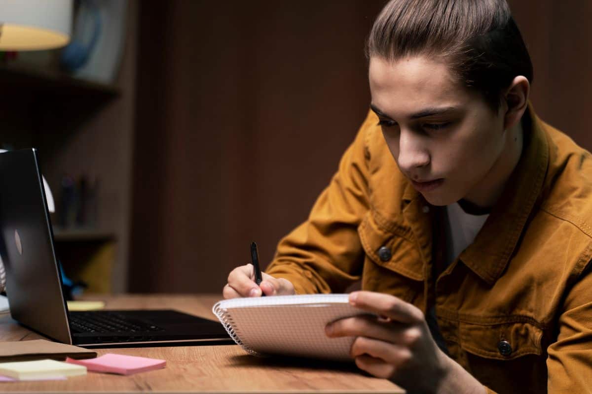 Teenage boy taking notes from laptop at home
