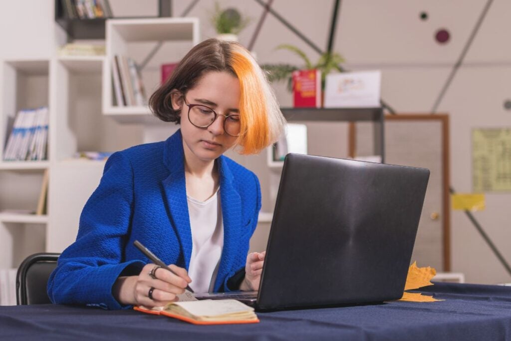 Pretty young girl in blue business suit sits at table with laptop