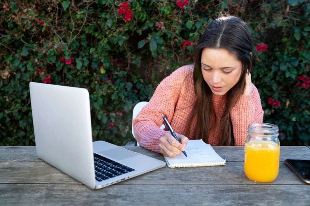 Young woman taking notes outdoors while using a laptop