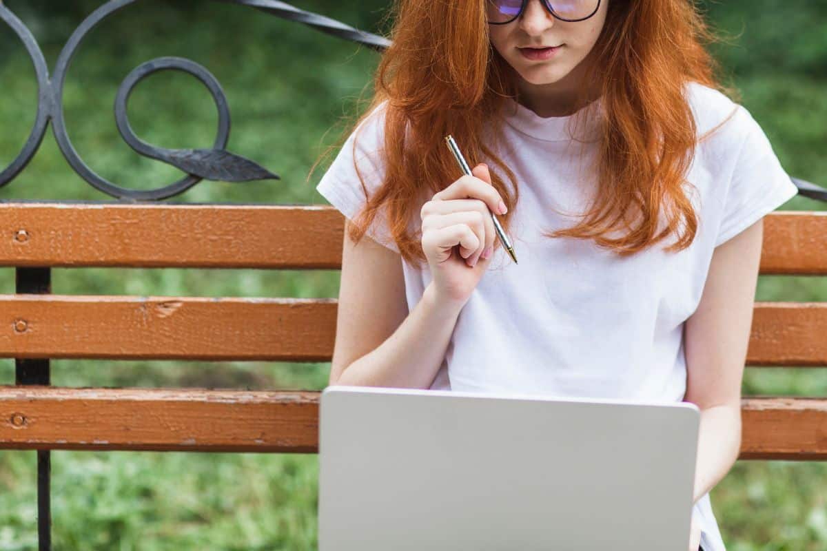 Mulher sentada num banco com um computador portátil e uma caneta