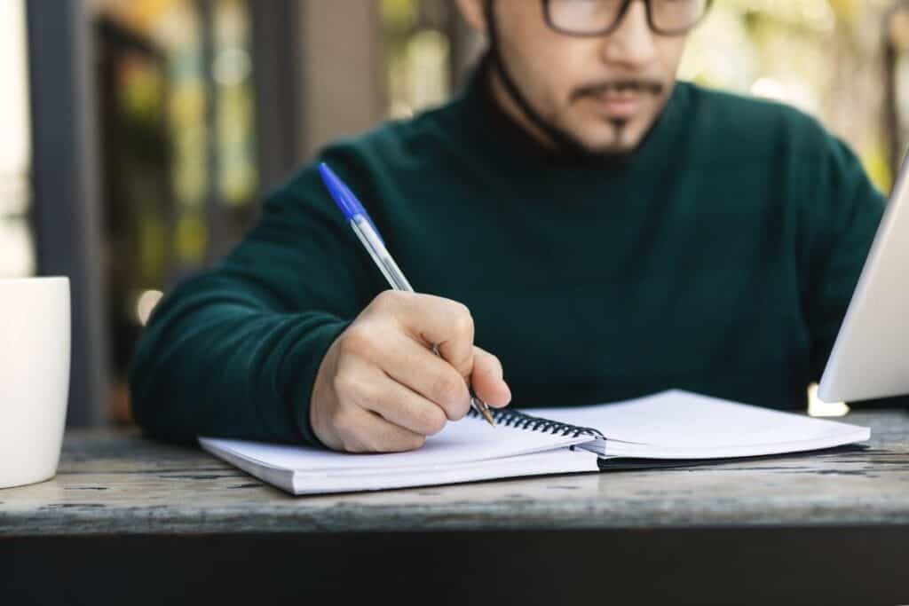 Man writing in notebook focused on work writing with pen
