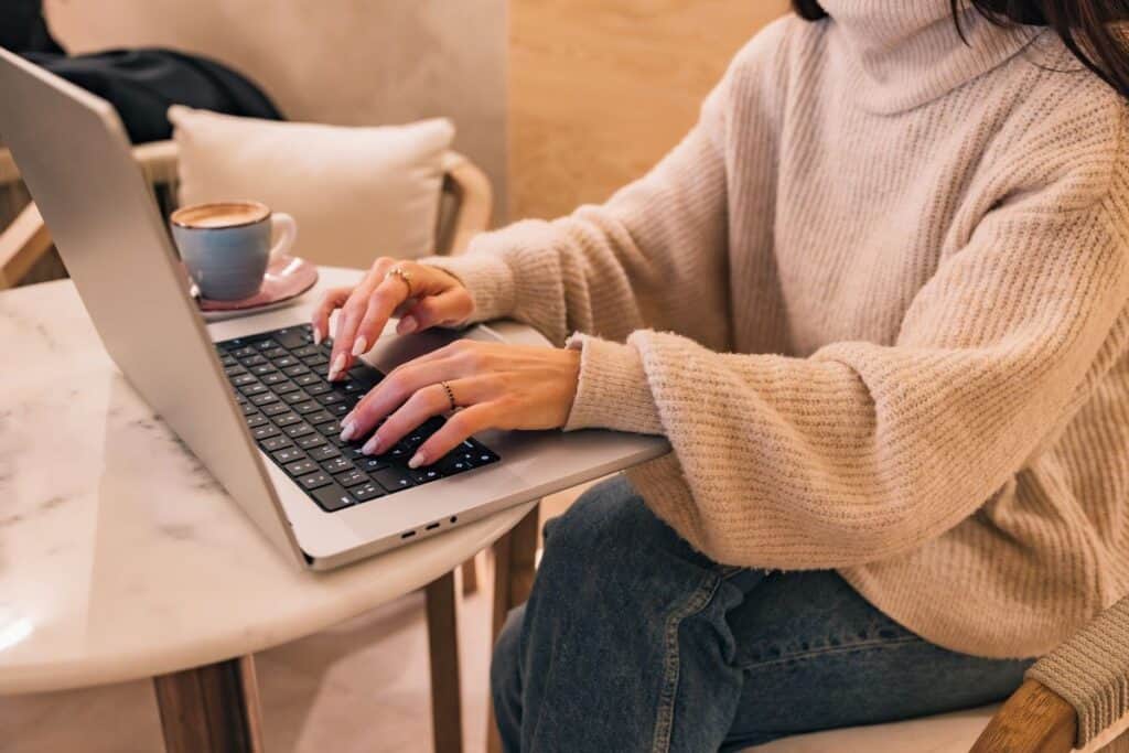 Woman typing on laptop in cafe working remotely