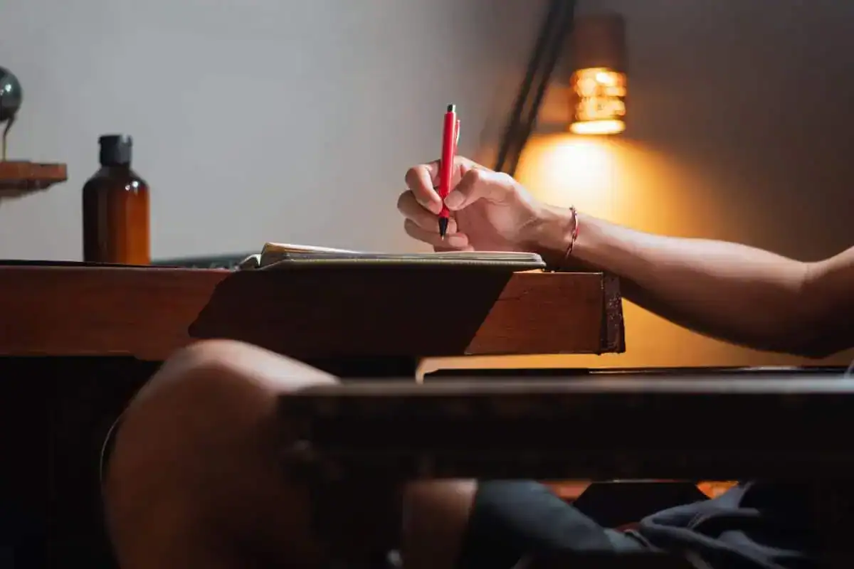 Person writing in notebook at wooden desk