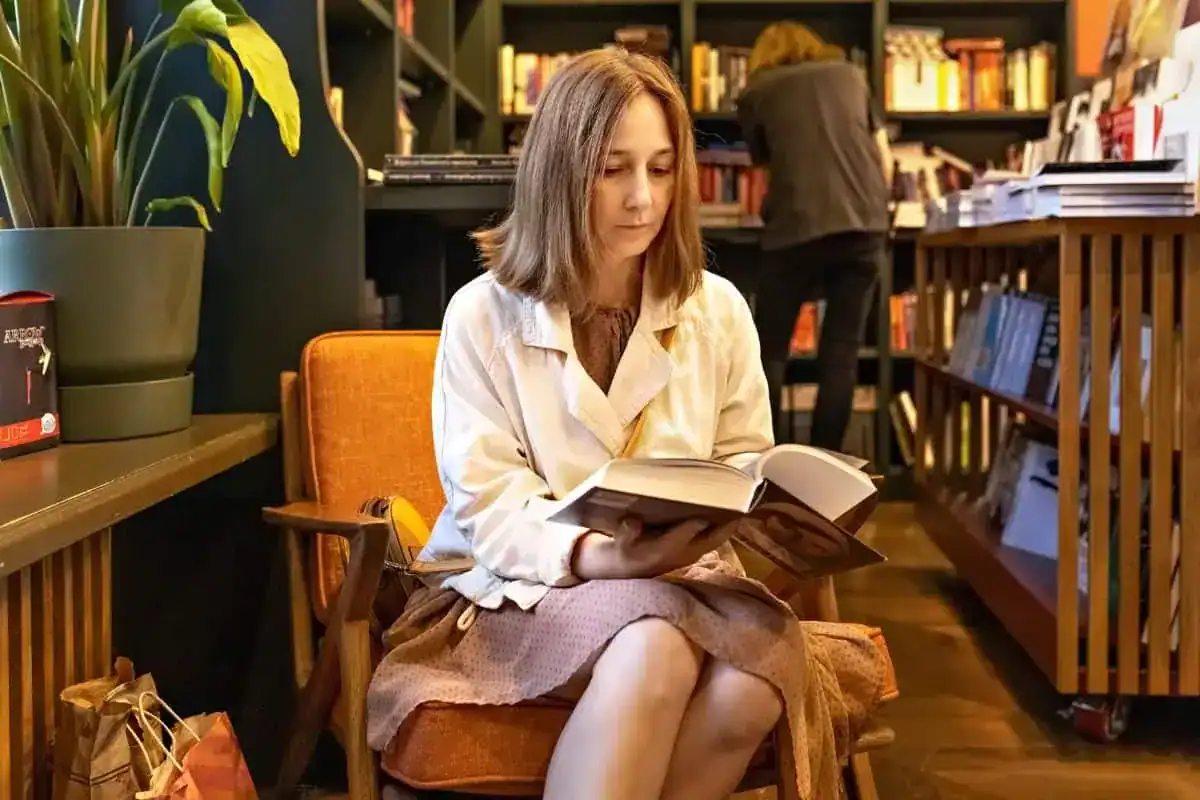 A young woman a student is sitting in the library reading a book college life