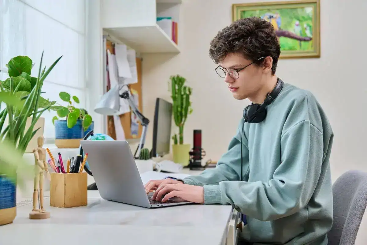 Young male college student sitting at desk at home using laptop