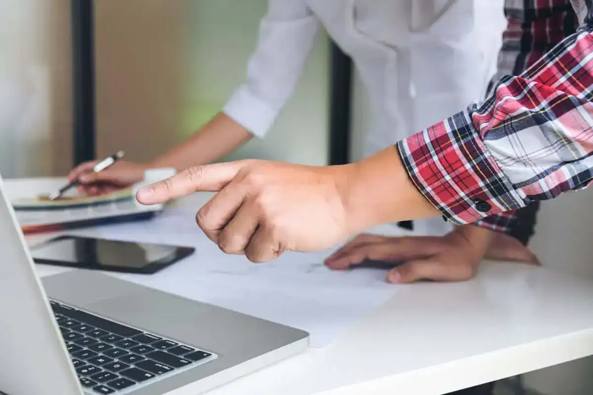 Midsection of colleagues using laptop at desk in office