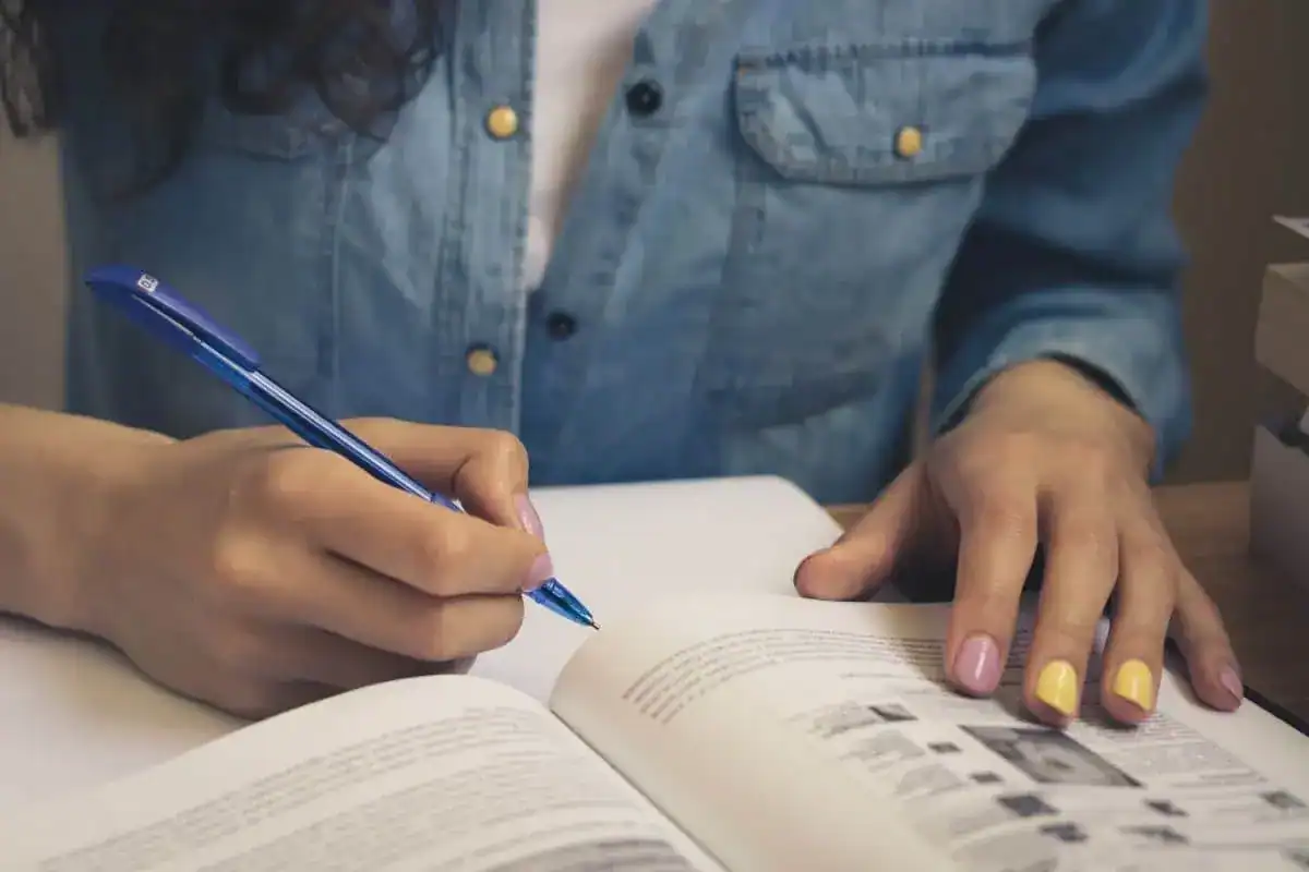 Girl in a denim shirt reading a textbook and taking notes