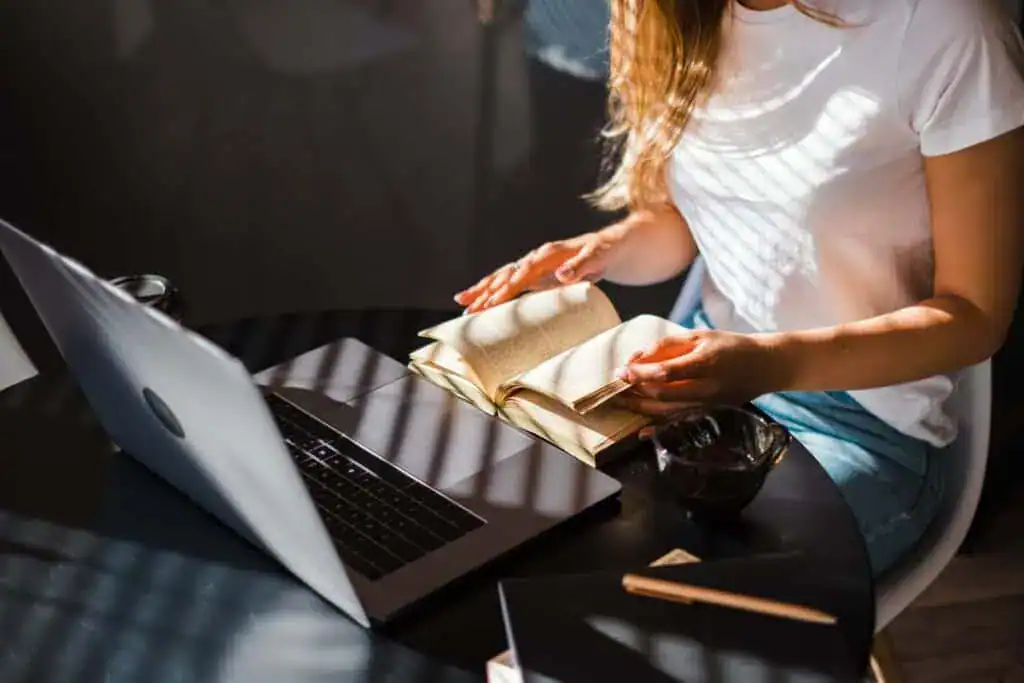 woman reading book in front laptop at the kitchen