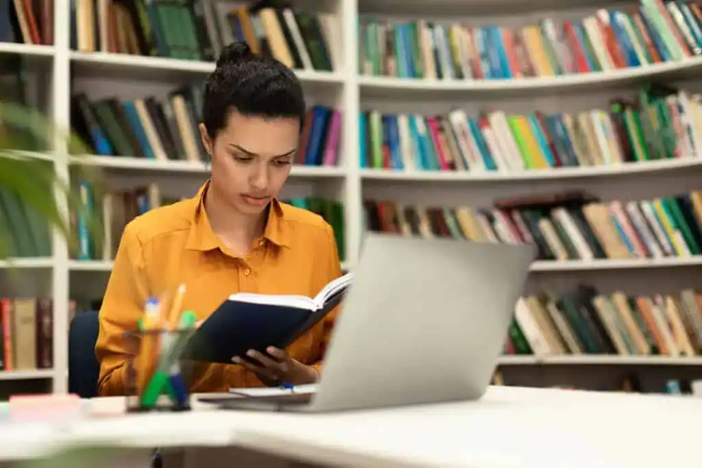 Concentrated mixed race woman reading book sitting in library