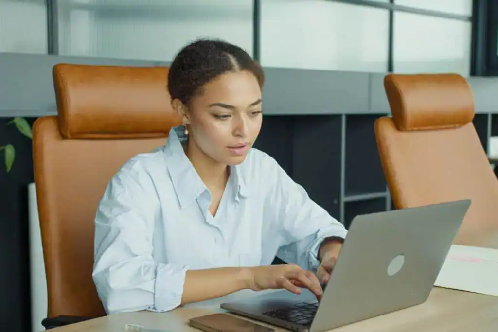 A focused young woman working on a laptop in a modern office environment