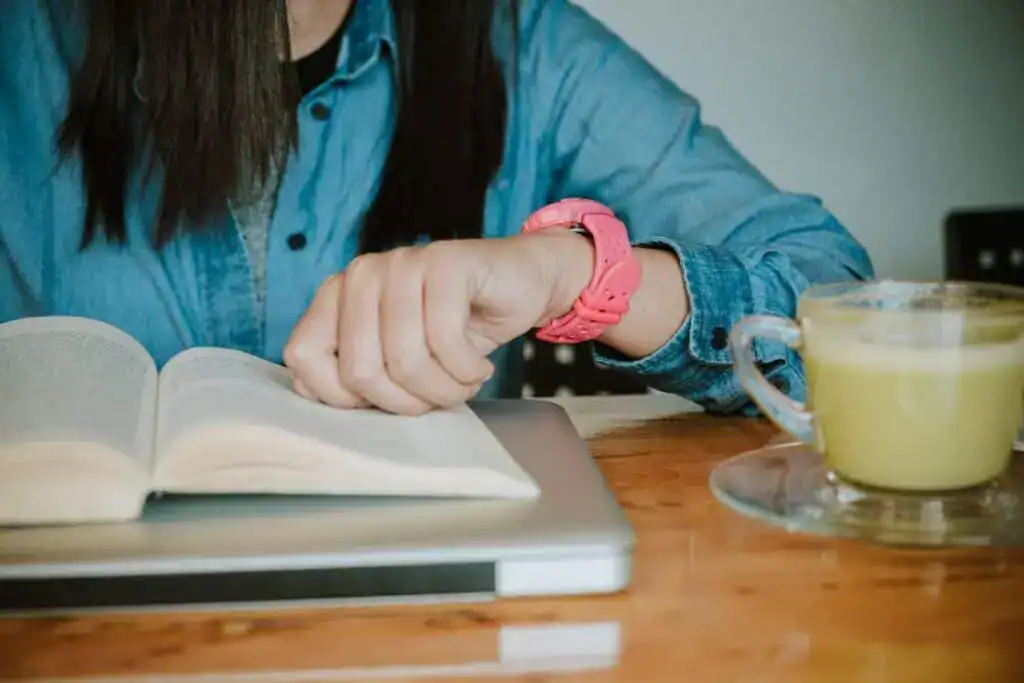 Hands of young woman looking at watch while reading a book